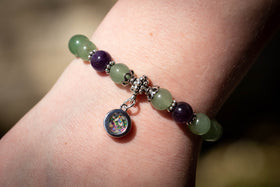 Photo depicts the aventurine and amethyst bracelet on a model's wrist. The dainty circle charm, made with green and dusk blue opal, faces towards the viewer. Aventurine bracelet, aventurine jewelry, amethyst bracelet, amethyst jewelry, natural stone jewelry, remembrance jewelry, jewelry for cremation ash, bracelet for ash