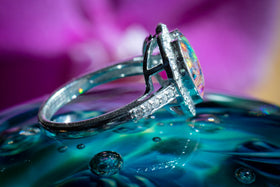 Side view of Bedazzled Heart Cremation Ring with rainbow selection of crushed opal. The ring is sitting atop a glass surface. Sterling Silver Ring for Ash, Sterling Silver Memorial Jewelry, Remembrance Jewelry, Silver Ring