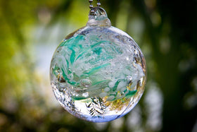 teal and white glimmer orb hanging outside in sun with  cremation ash